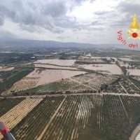 Veduta aerea di campi coltivati divisi da filari, horizonline distesa tra nuvole; un paesaggio rurale italiano.