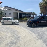 Auto e veicoli delle forze dell'ordine davanti a un'officina, contesto di riparazione veicoli e attività di servizio in un'area aperta.