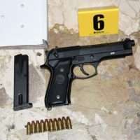 Pistola nera con caricatore staccato e sei munizioni spente su sfondo marmoreo, marcatura gialla con numero 6 in alto a destra.