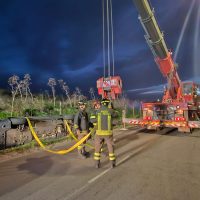 Squadre di soccorso all’opera di notte: vigili del fuoco con equipaggiamento, cavo giallo e mezzo pesante in azione su strada.