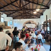 Ristorante affollato in un edificio rustico con tavoli apparecchiati, persone che chiacchiano e servizio al tavolo durante un evento.