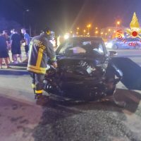 Incidente stradale notturno: auto frontalmente danneggiata, vigili del fuoco presenti e soccorritori in azione, luci delle emergenze tremolanti.