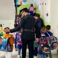 Insegnante o adulto guida un gruppo di bambini a scuola; immagine di corridoio colorato con zaini, colori vivaci e decorazioni murali.