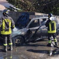 Vigili del fuoco in adottopresente vicino a un furgone parzialmente bruciato, sul luogo dell’incendio stradale, in strada bagnata.