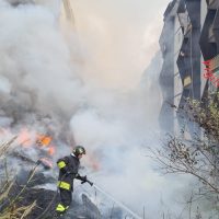 Incendio in un edificio urbano, fumo denso e fiamme visibili mentre i vigili del fuoco intervengono in extremis.