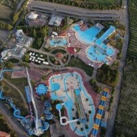 Veduta aerea di parco acquatico con piscine azzurre, scivoli colorati e percorsi d'acqua circondati da verde e strutture ricreative.