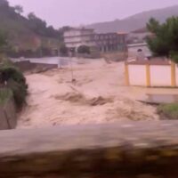 Paesaggio urbano durante un'alluvione: strade allagate, edifici sullo sfondo, fango e detriti, atmosfera di emergenza.