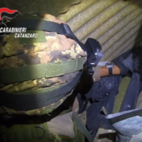 Carabiniere in uniforme mimetico osserva un ingresso o nascondiglio, tuta tattica, scena interna, atmosfera di operazione