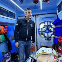 Medico in ambulanza, uomo in giacca scura all’interno, attrezzature sanitarie visibili, ambiente luminoso e strutturato, pronta assistenza.