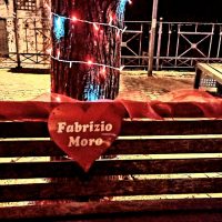 Cuore rosso con scritta Fabrizio Mone appoggiato su gradini, luci colorate e scena notturna sullo sfondo.