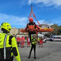 Soccorritori addestrano una squadra vicino a una barella trasportata da una gru. personale in alta visibilità in allerta, assistenza in esterna.