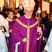 Cardinale vestito di viola con mitria, andanda dorata, camminando tra fedeli in chiesa, gremita di persone.