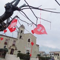 Cuori rossi appesi a rami spogli, davanti a una chiesa di fronte al cielo grigio, atmosfera romantica e nostalgica.