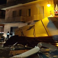 Nave da diporto incagliata al riparo di sedie e tavoli rovesciate, registrando una scena notturna di emergenza in una strada urbana.