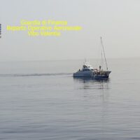 Barca a vela in mare aperto, delicati riflessi azzurri, testo giallo in alto a sinistra: descrizione minima di una scena marina serena.