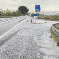 Strada innevata e scivolosa con cartelli stradali in prossimità di una curva, paesaggio rurale e cielo nuvoloso.