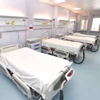 Sala ospedaliera con letti separati, biancheria bianca, luci naturali e attrezzature mediche, ambiente pulito e ordinato.