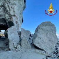 Scorcio di rocce grige e crumble con cielo azzurro, logo dei Vigili del Fuoco in alto a destra