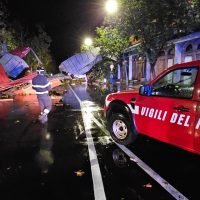 Intervento notturno dei vigili del fuoco su strada allagata, mezzi incendiati e personale al lavoro tra luci e ombre.