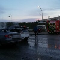 autovetture parcheggiate bagnate, vigili del fuoco e persone sul posto, in una strada allagata al tramonto