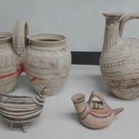 Vasi e anfore di ceramica beige con motivi geometrici, disposti su fondo chiaro.
