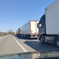 Autocarri in fila lungo una strada, guidati su corsia laterale con cielo sereno e paesaggio desertico.