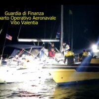 Immagine di una operazione notturna: barche illuminate sul mare con soccorritori e moto al largo, testo in alto a sinistra.