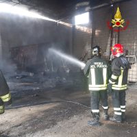 Incendio in corso: vigili del fuoco in tuta protettiva spegnono le fiamme con idranti, fumo e luce sparata dall’operazione.