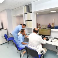 Medici in laboratorio osservano strumenti e monitor, lavorando in ufficio clinico moderno luminoso con scaffali e sedie blu.
