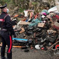Vigile urbano osserva cumulo di rifiuti e macerie, scenario di emergenza che suggerisce soccorso e gestione del disastro.