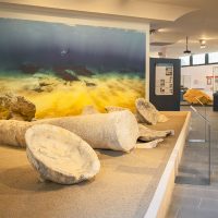 Interno luminoso in stile showroom con grandi rocce bianche su un tavolo e sfondo marina: immagini di sabbia e cielo.
