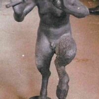 Figura di cavallo scolpito in pietra, statica, con dettagli muscolari e coda corta, tono grigio scuro su sfondo neutro.