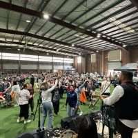 Concerto all'aperto in palestra, pubblico felice danzante tra luci soffuse e band in scena, atmosfera vivace e comunitaria.