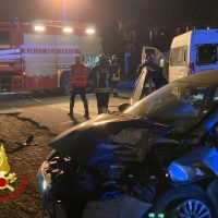Autovettura coinvolta in incidente stradale notturno su strada urbana; vigili del fuoco e soccorritori presenti, mezzi di emergenza all'opera.