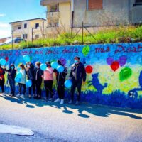 Gruppo di persone davanti a una parete dipinta con cuori colorati e messaggi, in un ambiente urbano.