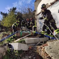 Equipe di vigili del fuoco al lavoro su una voragine fuori strada, tra macerie e cavi, in un contesto urbano.