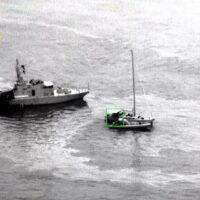 Due imbarcazioni sulla superficie dell'acqua, una piccola barca a vela verde tra una nave di pattuglia a sinistra.