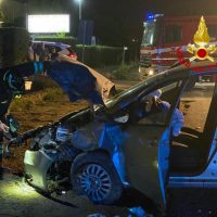 Auto incidentata di notte: conducente estratto dall’abitacolo da soccorsi, finestrini rotti, lampeggianti blu e ambulanza sullo sfondo.