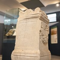 Scultura antica in pietra, tonda: rilievi e iscrizioni sul frontale, esposizione museale con vetrine sullo sfondo