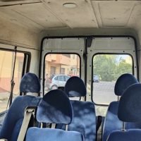 Interni di un minivan con sedili blu, posti a sedere in fila, finestra aperta e luce esterna verso una strada.