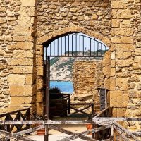 Antica finestra di pietra con vista sul mare, ferro battuto e tavole in legno, paesaggio costiero tra rocciose mura architettoniche