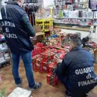Due ufficiali delle Fiamme Gialle esaminano scaffali di dolci confezionati in un negozio, monitorando la merce in esposizione.