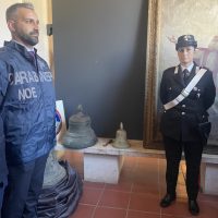 Due uomini in divisa vicino al grande ritratto, uno in abiti di polizia e l'altro in uniforme militare, in una sala con statue e scaffali sullo sfondo.