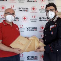 Due uomini, uno in soccorso civile rosso e l’altro in uniforme, scambiano un documento su sfondo con logo ‘Un’Italia che المزيد’.