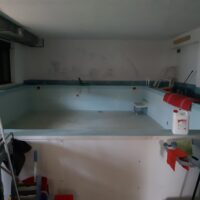 Piscina interna vuota, pareti bianche, luci soffuse, scale e attrezzature da piscina lungo il perimetro.