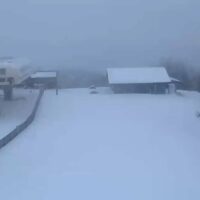 Paesaggio innevato incolto con edifici e strada avvolti dalla nebbia, tonalità azzurrine e neve fresca diffusa.