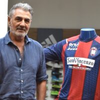 Imprenditore con camicia blu accanto a una maglia da calcio colorata, sfondo di negozio e scaffali