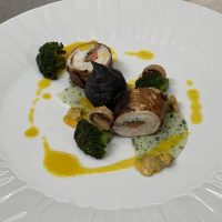 Insalata di filetto di pesce avvolto in pancetta, accompagnata da broccoli e salsa gialla, presentata su grande piatto bianco.