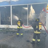 Due pompieri con tuta antincendio e manicotti, in azione vicino a un edificio in fiamme e vetri crepati, durante un soccorso