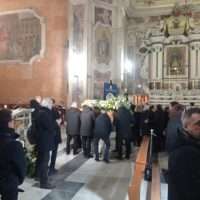 Gruppo di persone in chiesa, aiuole, architettura sacra gotica e ornamenti dorati, atmosfera solemne durante una funzione religiosa.